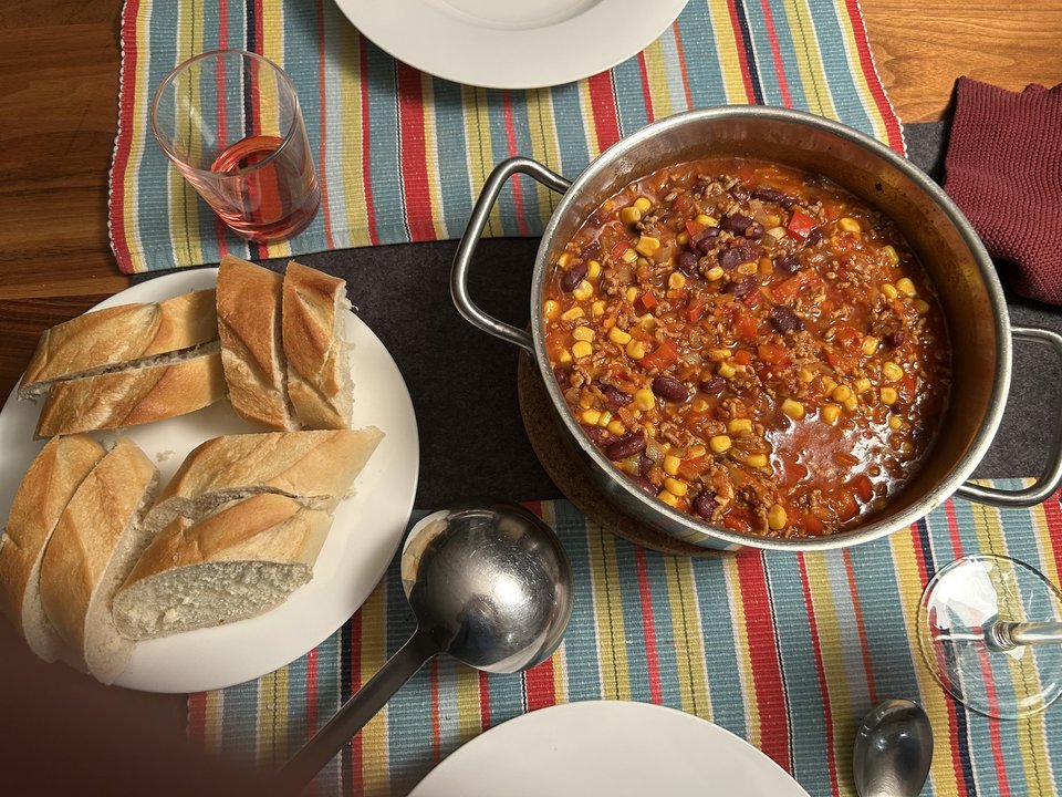 Fertiges Chili con Carne im Topf auf einem gedeckten Tisch mit einem Teller Baguette