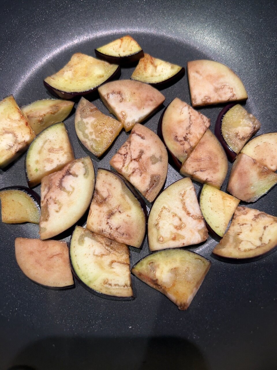 Auberginenstücke beim kräftigen Anbraten im Wok