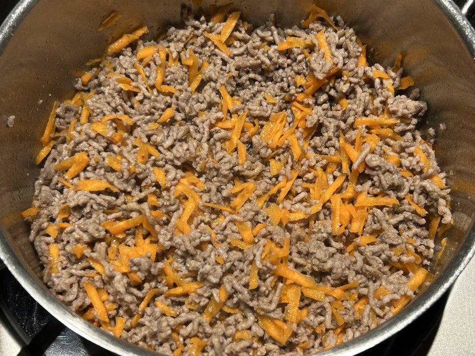 Krümeliges Hackfleisch mit grob geraspelter Möhre in einem Edelstahltopf