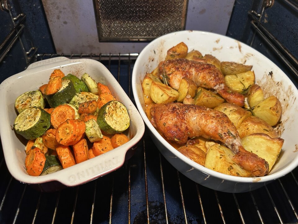 Zwei Auflaufformen mit gebackenem Hähnchen, Kartoffeln, Karotten und Zucchini im Ofen